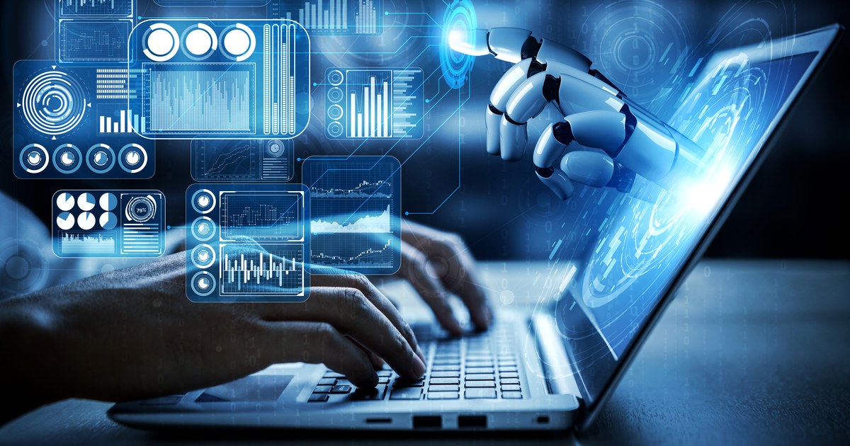 A robotic hand reaching toward a laptop screen surrounded by floating data dashboards while a person types.